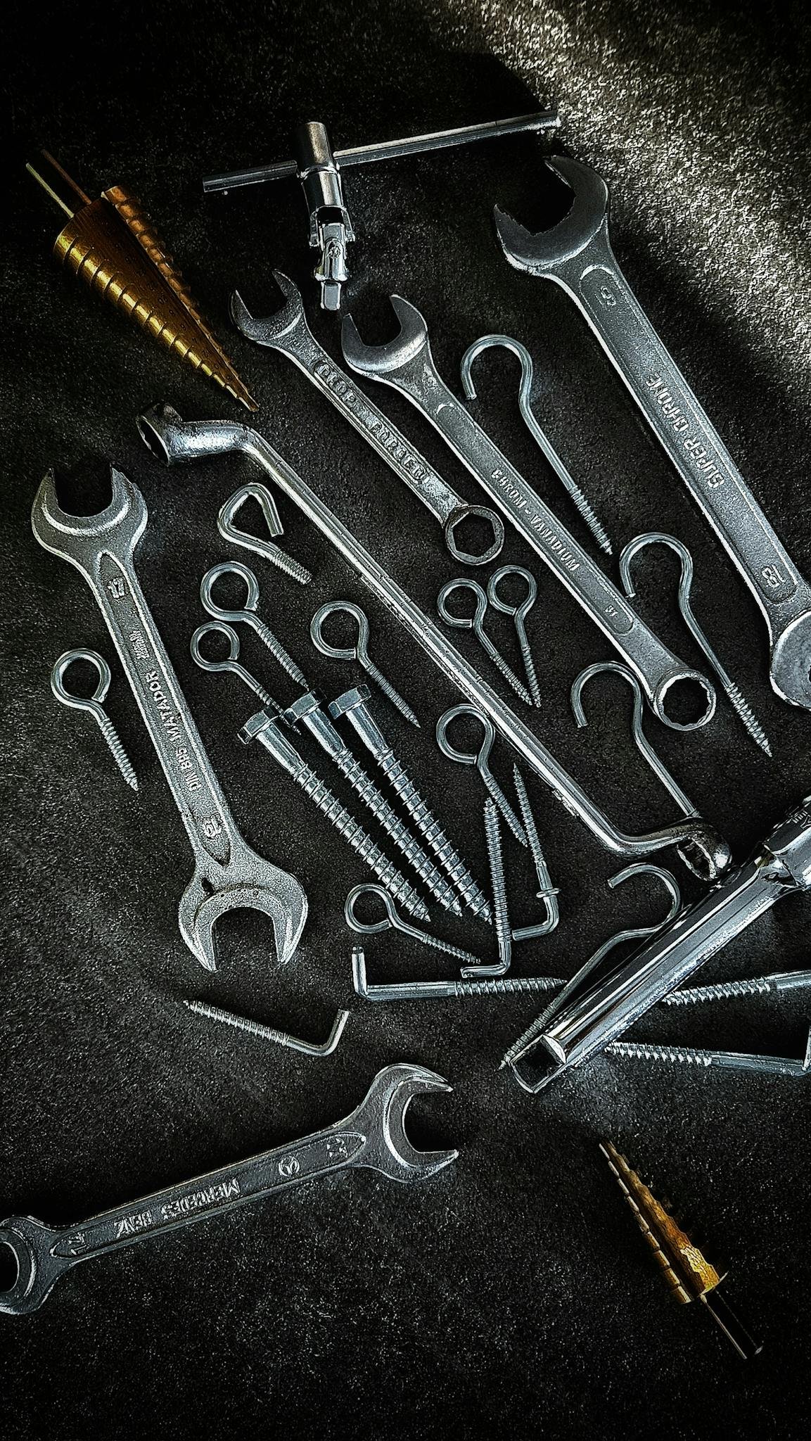 A collection of metal tools including wrenches and screws arranged on a dark background.