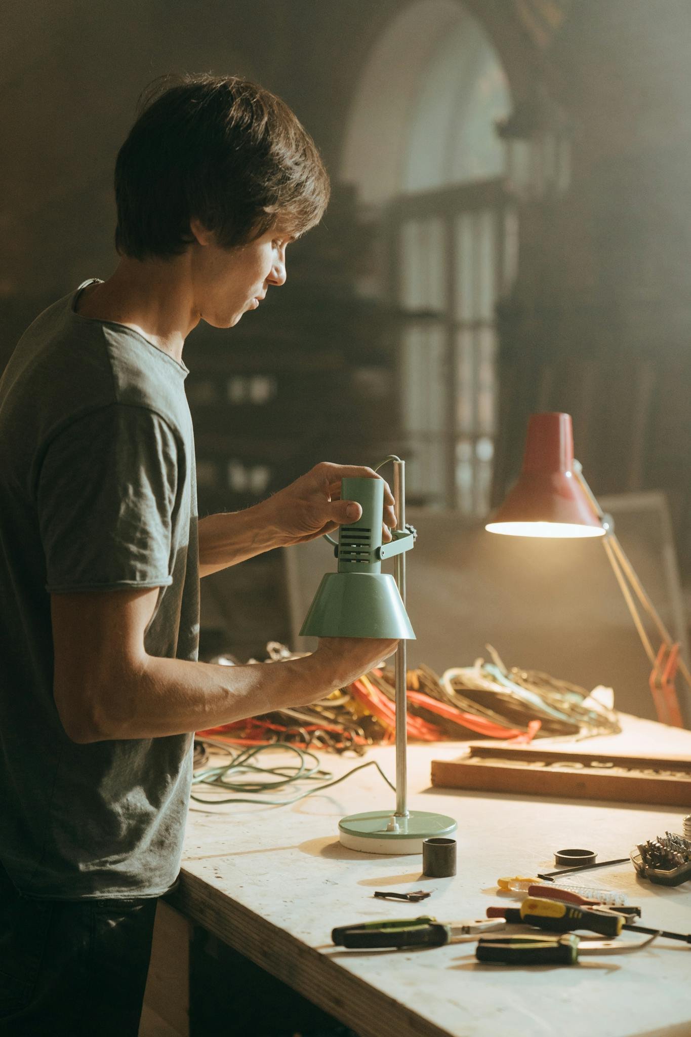 A man in a workshop assembles a lamp amidst tools and equipment.