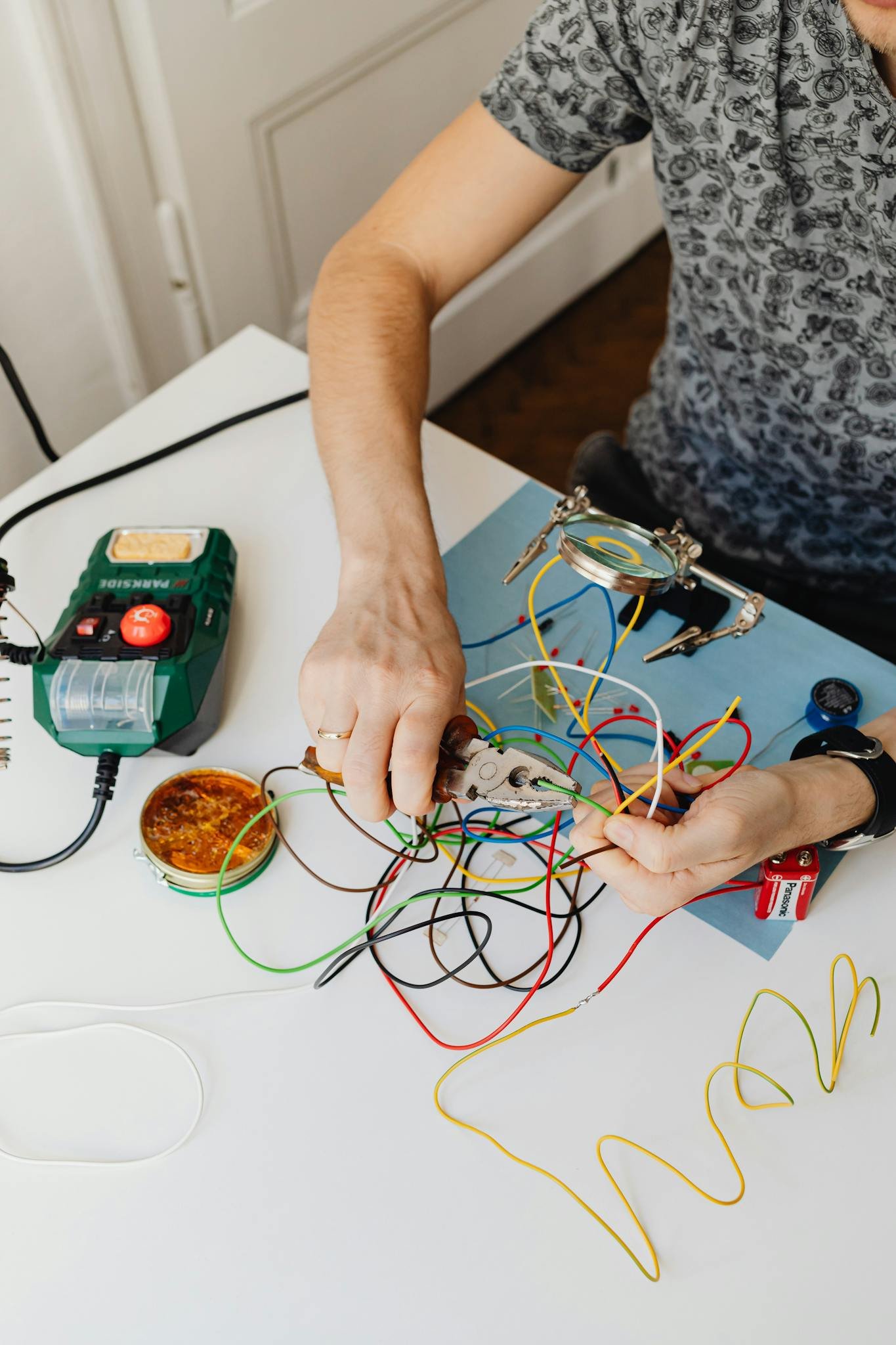 Close-up of hands working on electronic circuit with pliers and colorful wires.