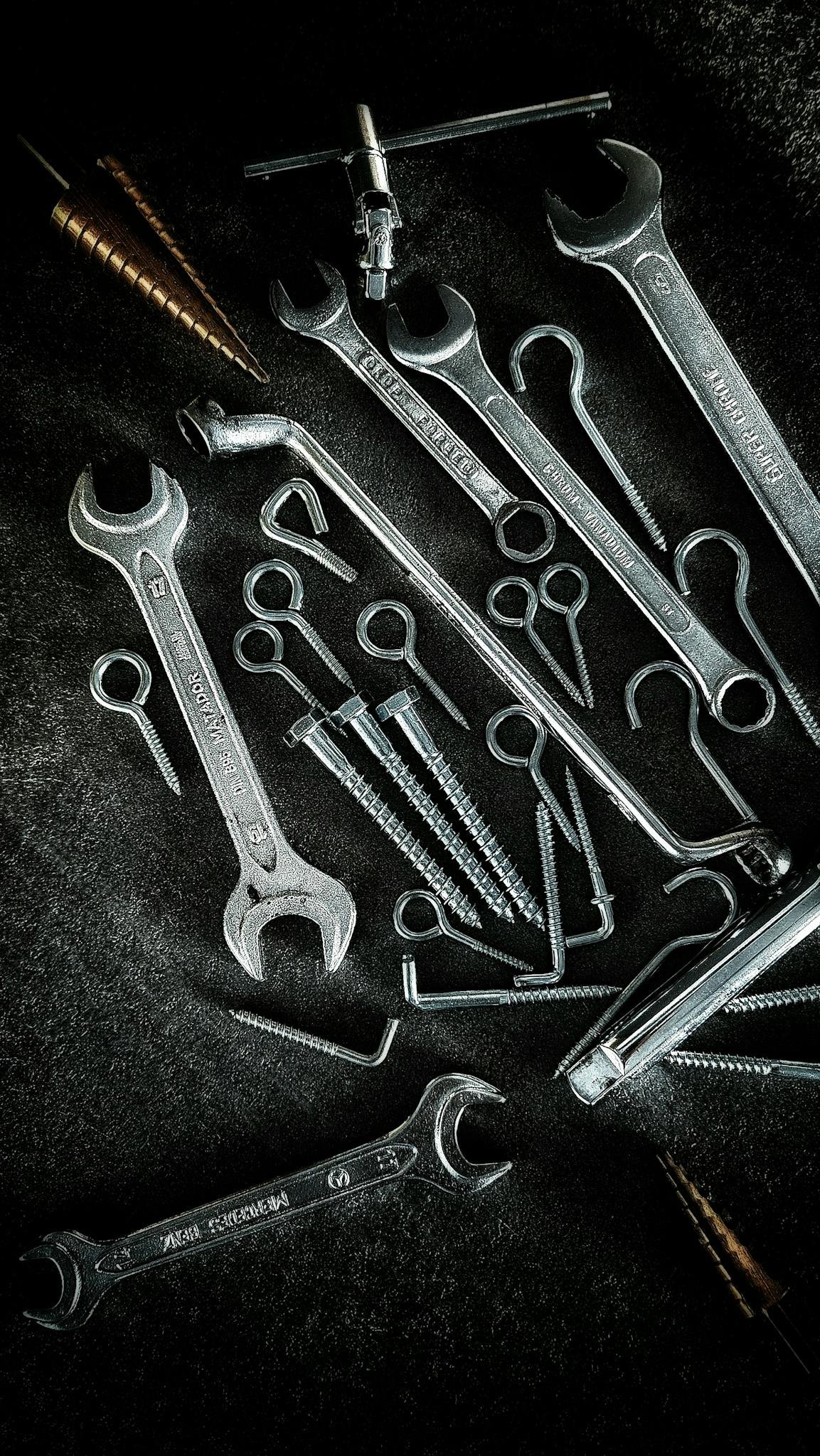 Collection of metal tools including wrenches and screws on a textured surface, ideal for DIY and repair themes.